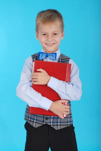 Menino de uniforme escolar segurando um livro vermelho — Fotografia de Stock