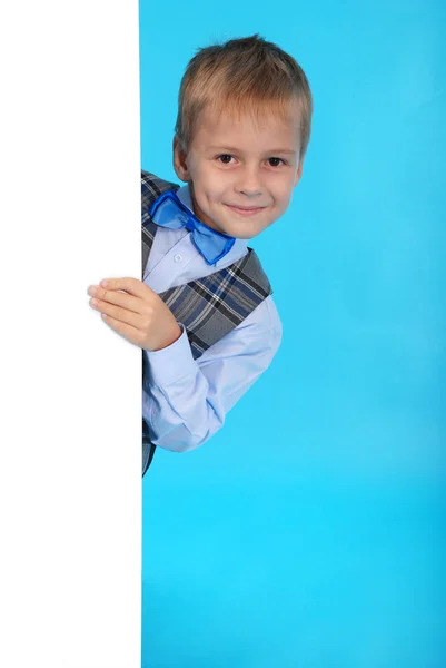 Een lachende schooljongen poseren achter een witte reclamebord — Stockfoto