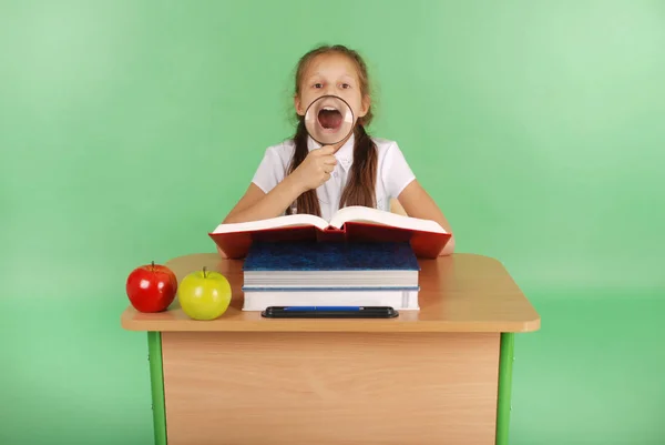 Chica en uniforme escolar sentada en un escritorio con una lupa — Foto de Stock