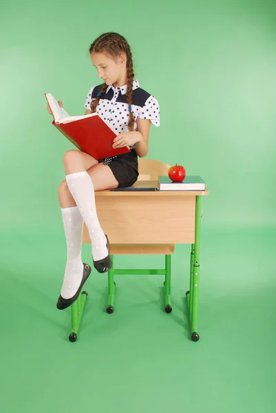 Holka ve školní uniformě sedí na stole a čtení knihy — Stock fotografie