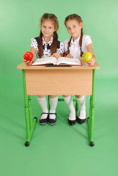 Две девушки в школьной форме сидят за столом и читают книгу — стоковое фото