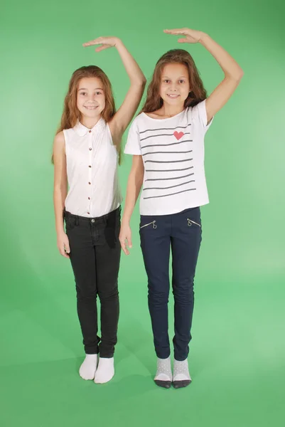 Dos niñas de la escuela toman las manos por encima de la cabeza y miden su crecimiento — Foto de Stock