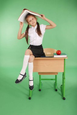 Eğitim, insanlar, çocuklar ve okul kavramı - başında bir kitapla masada oturan genç liseli kız