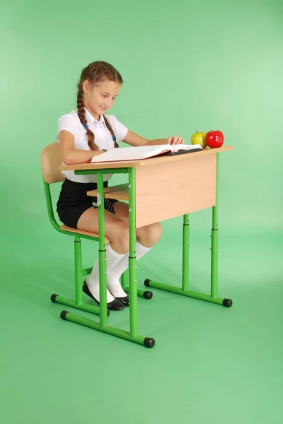 Dívka ve školní uniformě sedí u stolu a čtení knihy — Stock fotografie