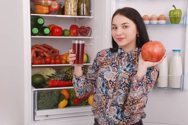 Güzel gülümseyen genç kız bir bardak nar suyu ve garnet buzdolabı arka plan üzerinde tutar.