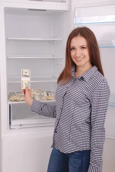 Jovencita sosteniendo dólares en el fondo del refrigerador . — Foto de Stock