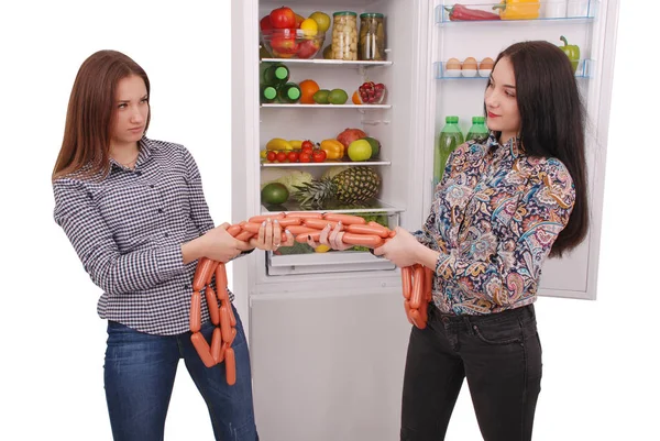 Duas meninas mantém salsichas no fundo da geladeira — Fotografia de Stock