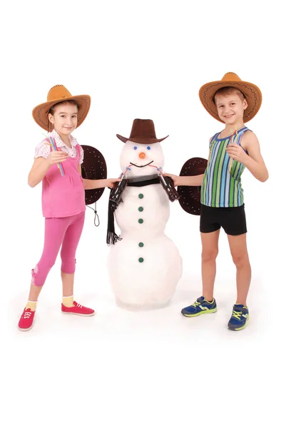 Lindo chico y chica sosteniendo una botella de cola cerca de un muñeco de nieve con bufanda y sombrero — Foto de Stock