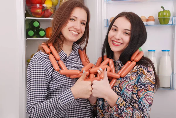 İki genç kız tutar sosis buzdolabı arka plan üzerinde