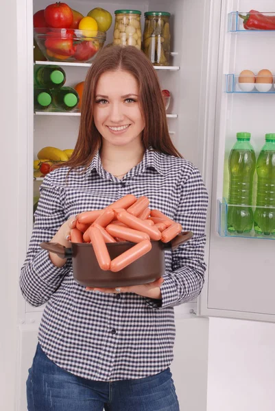 Jovencita sostiene salchichas en el fondo del refrigerador — Foto de Stock