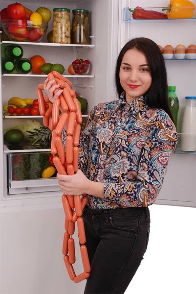 Genç kız sosis buzdolabı arka plan üzerinde tutar.