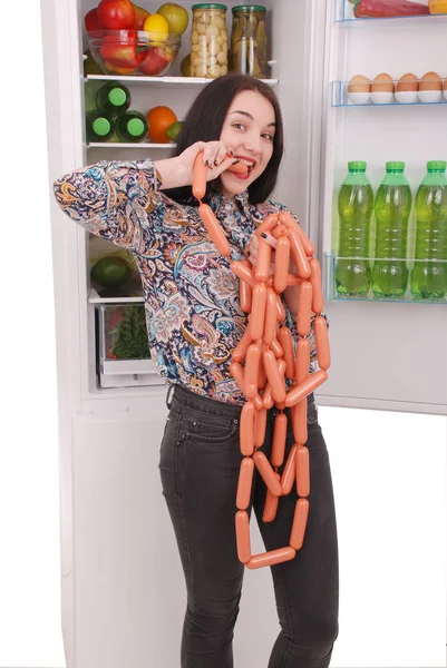 Genç kız sosis buzdolabı arka plan üzerinde tutar.