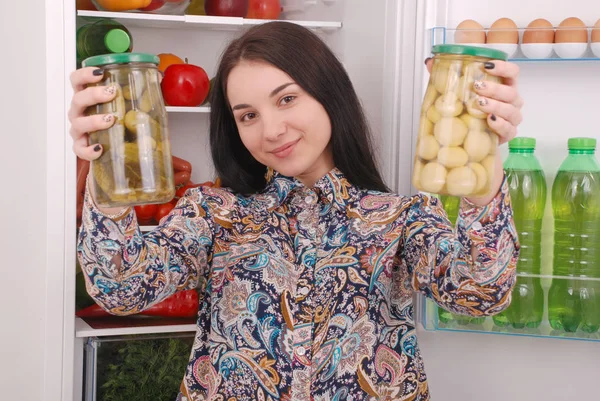 Genç kız tutun konserve petrol ve salatalık buzdolabı arka plan üzerinde