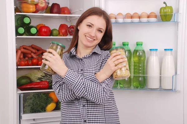 Genç kız tutun konserve petrol ve salatalık buzdolabı arka plan üzerinde