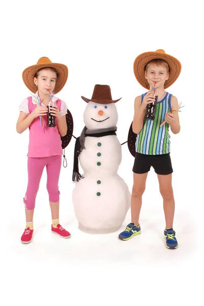 Cute boy and girl holding a cola bottle near a snowman with scarf and hat — Stock Photo, Image