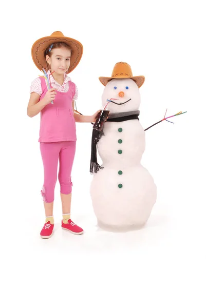 Linda chica sosteniendo una botella de cola cerca de un muñeco de nieve con bufanda y sombrero — Foto de Stock