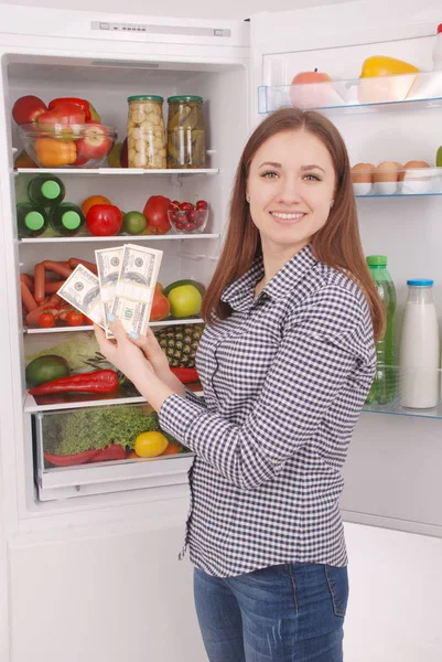 Jong meisje dollar te houden op de achtergrond van de koelkast. — Stockfoto