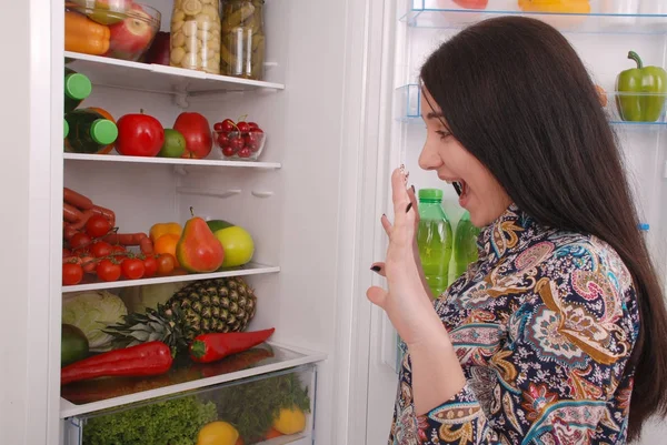 Jong meisje met een geamuseerd gezicht op de achtergrond van de koelkast — Stockfoto