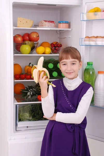 Girl is holding a banana on the refrigerator background. — Stock Photo, Image