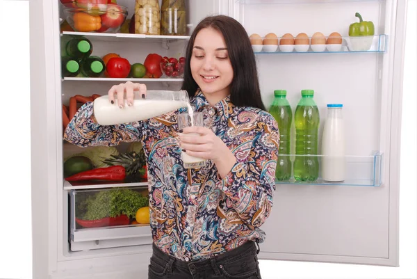 Jovencita sostener botella de leche, de pie cerca de la nevera abierta — Foto de Stock