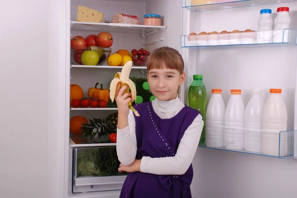 Menina está segurando uma banana no fundo da geladeira . — Fotografia de Stock