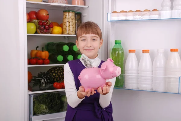 돼지 저금통 (돈 상자) 냉장고 배경에 서 있는 여자 — 스톡 사진