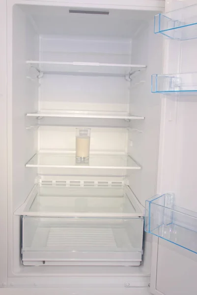Glass of milk inside in empty clean refrigerator