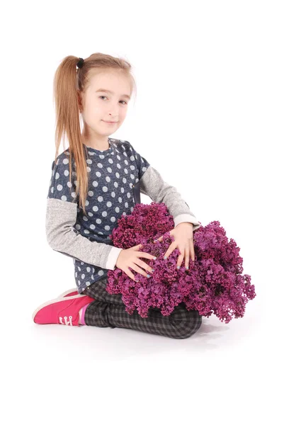 Chica atractiva sentada en el suelo blanco con lila en la mano — Foto de Stock