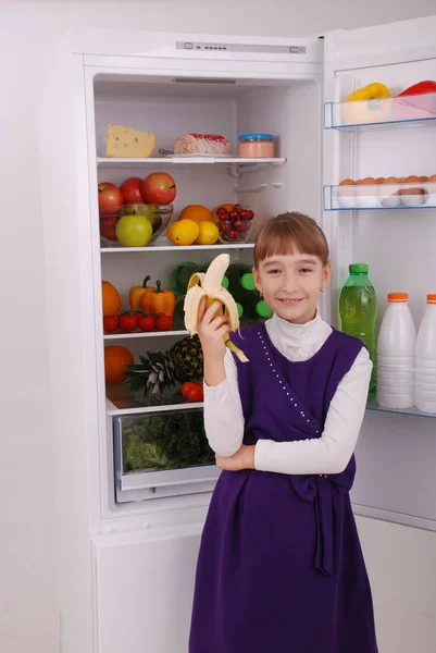 Meisje houdt een banaan op de achtergrond van de koelkast. — Stockfoto