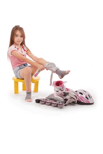 Encantadora chica de pelo broun de la edad escolar en pantalones cortos vaqueros y una camiseta rosa sentada en la silla e intenta patinar . — Foto de Stock