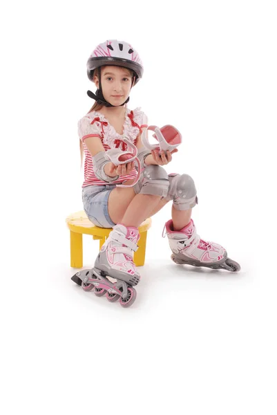 Affascinante ragazza dai capelli corti in età scolare in pantaloncini jeans corti e una t-shirt rosa seduta sulla sedia e cerca di piedi pattini a rotelle . — Foto Stock