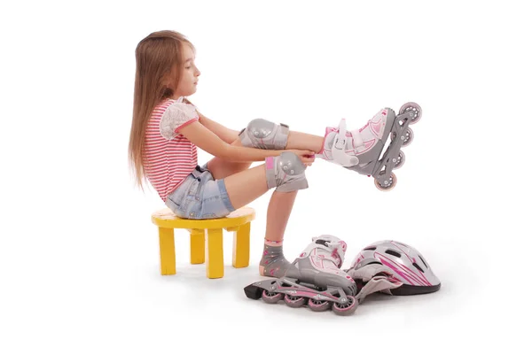 Charmantes braunhaariges Mädchen im Schulalter in kurzen Jeans-Shorts und rosa T-Shirt sitzt auf dem Stuhl und versucht, Rollschuhe zu Fuß zu gehen. — Stockfoto