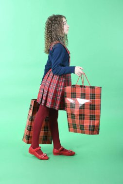 Yeşil arka planda yalıtılmış kırmızı bir paket olan çocuk. Küçük güzellik alışverişkolik. Tatil hediyesi, alışveriş. 