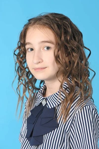 Portret adorable uśmiechniętą uczennicę z włosów Curl, stojący izolowane na niebieskim tle. — Zdjęcie stockowe