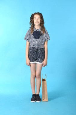 Mavi arka planda izole edilmiş bir paketolan çocuk. Tatil hediyesi, alışveriş. Alışveriş merkezinde çocuk mutlu alışveriş. 