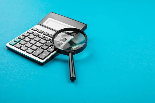 Calculator en vergrootglas op blauwe achtergrond. — Stockfoto