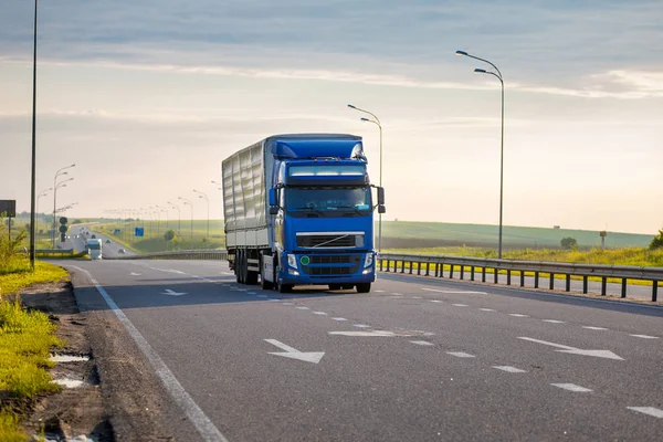 Aankomst blauwe vrachtwagen op de weg in een landelijk landschap bij zonsondergang — Stockfoto