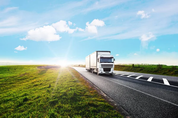 Aankomst witte vrachtwagen op de weg in een landelijk landschap bij zonsondergang — Stockfoto