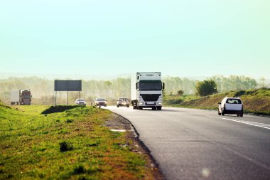 Gün batımında kırsal bir arazide beyaz bir kamyon geliyor.