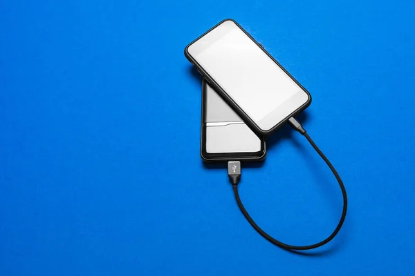 Black Power bank charges smartphone isolated on blue background — Stock Photo, Image