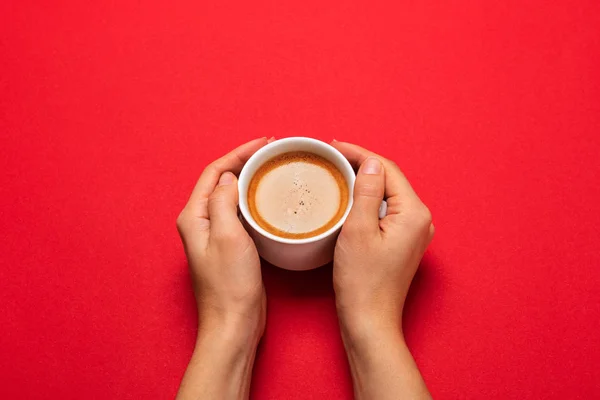 Γυναικείο χέρι που κρατά ένα λευκό κύπελλο με μαύρο καφέ σε ένα κόκκινο backg — Φωτογραφία Αρχείου