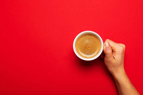 Weibliche Hand hält eine weiße Tasse mit schwarzem Kaffee auf rotem Rücken — Stockfoto