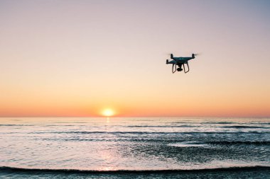 Deniz günbatımının arka planında uçan dron