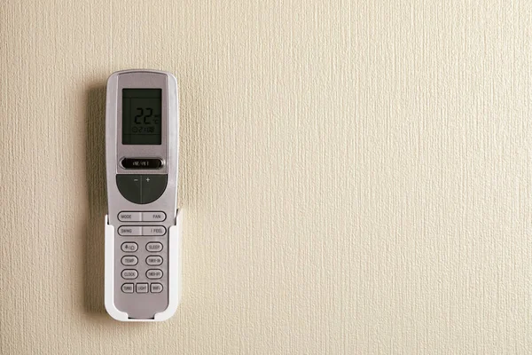 Air conditioner remote control on white concrete wall.