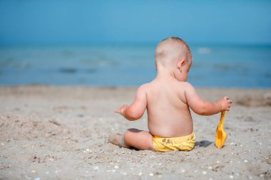 Küçük çocuk deniz kenarında kumla oynuyor.