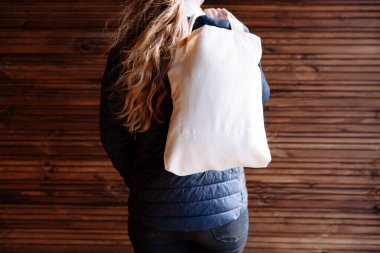 Ahşap arka planda beyaz tekstil eko çantası tutan genç bir kadın.