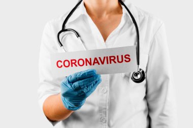 Coronavirus, üzerinde Coronavirus yazan beyaz kart beyaz önlüklü ve eldivenli doktorun ellerinde.. 