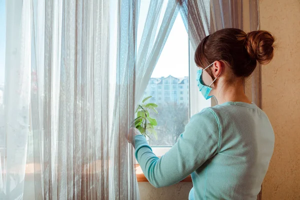 仮面の少女が窓の外を見てる コロナウイルスと隔離の概念 — ストック写真