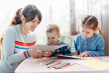 Çocuklu bir anne masada oturur ve ödev yapar. Çocuk evde öğreniyor. Evde eğitim.