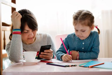 Kızı odada resim yaparken kadın cep telefonuyla çalışıyor.